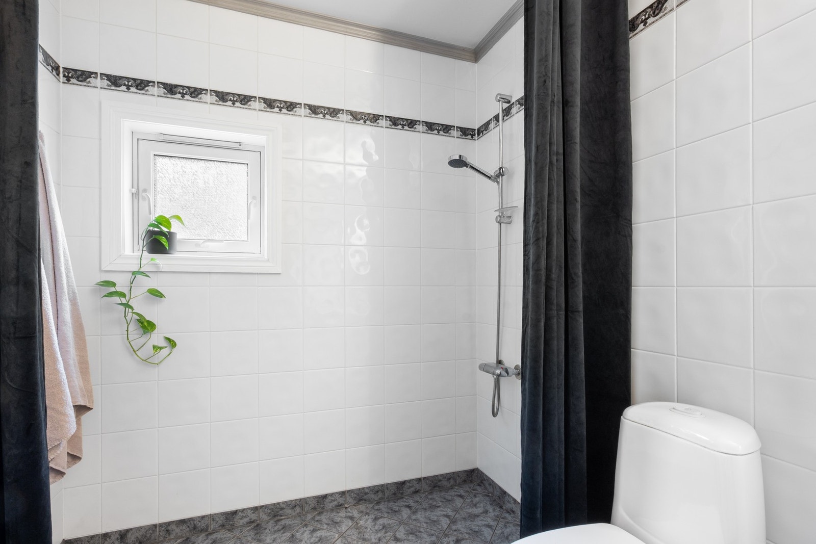 Badet er innredet med gulvmontert toalett, dusj med forheng, servantseksjon med skuffer og skap. Galleribilde