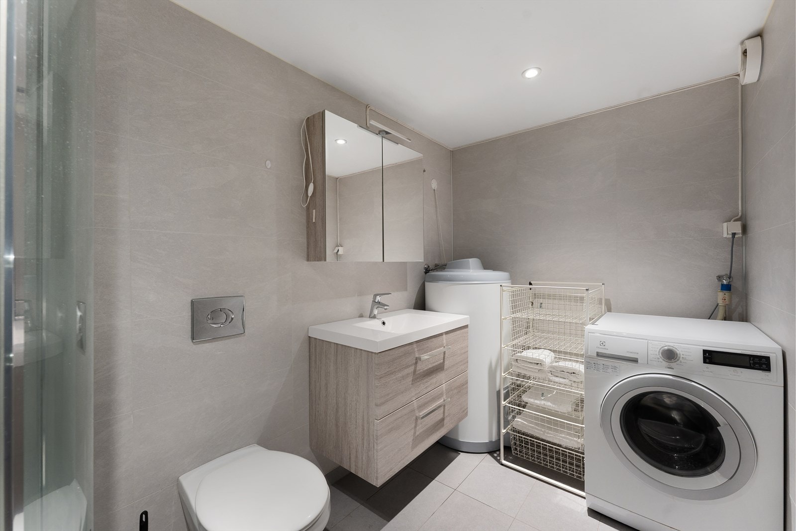 Badet har flislagt gulv med elektriske varmekabler. Badet har heldekkende servant, veggmontert toalett og dusjkabinett, samt opplegg for vaskemaskin. Galleribilde