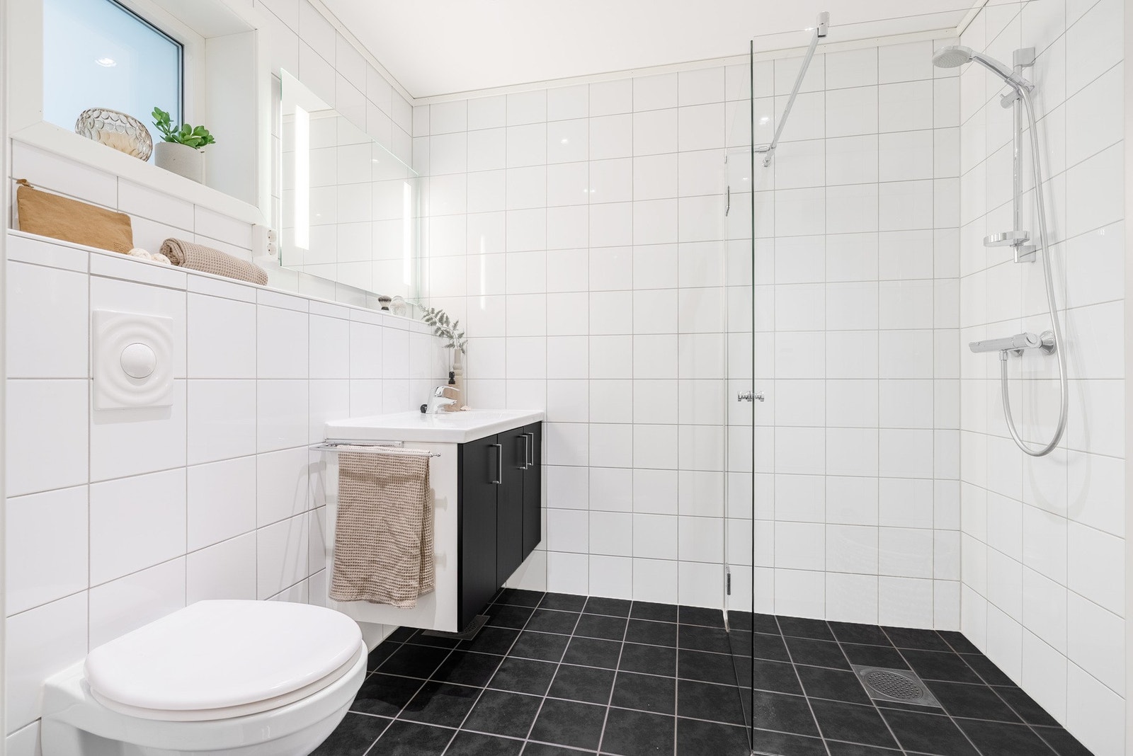 Leiligheten har to fullverdige bad. Dette badet er praktisk plassert i tilknytning til gangen og er innredet med dusj, vegghengt toalett, servant og behagelig gulvvarme. Badets plassering gjør at det er godt skjermet fra stue og kjøkken. Galleribilde