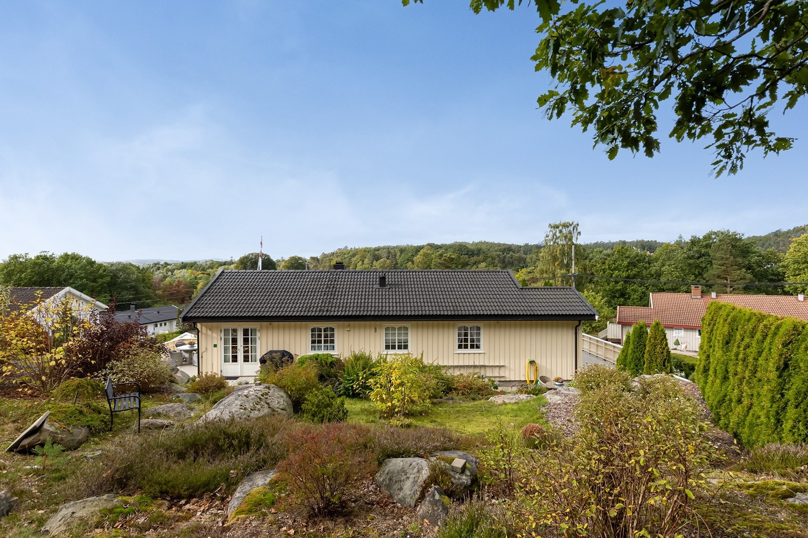 Eiendommen ligger fint til på en stor og grønn tomt med naturlige fjellpartier og frodig beplantning. Galleribilde