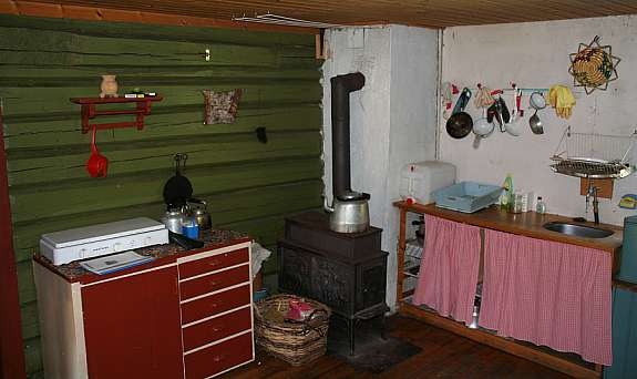 Kjøkken med vedovn, kokebluss og utslagsvask. Stua er bak tømmerveggen. Galleribilde