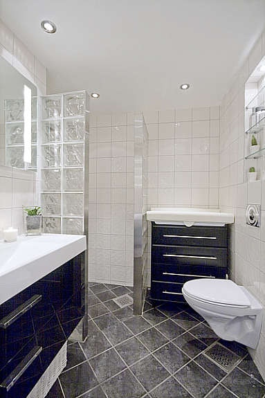 Lekkert flislagt bad med høy standard som er utstyrt med hvit vegghengt WC, heldekkende servant med servantskap og dusjnisje med glassbyggerstein. Galleribilde