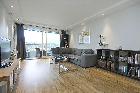 Stuen er romslig med mye lys inn fra de store vinduene mot balkongen. Eikeparkett på gulvet og veggene er sparklet og malt. Galleribilde