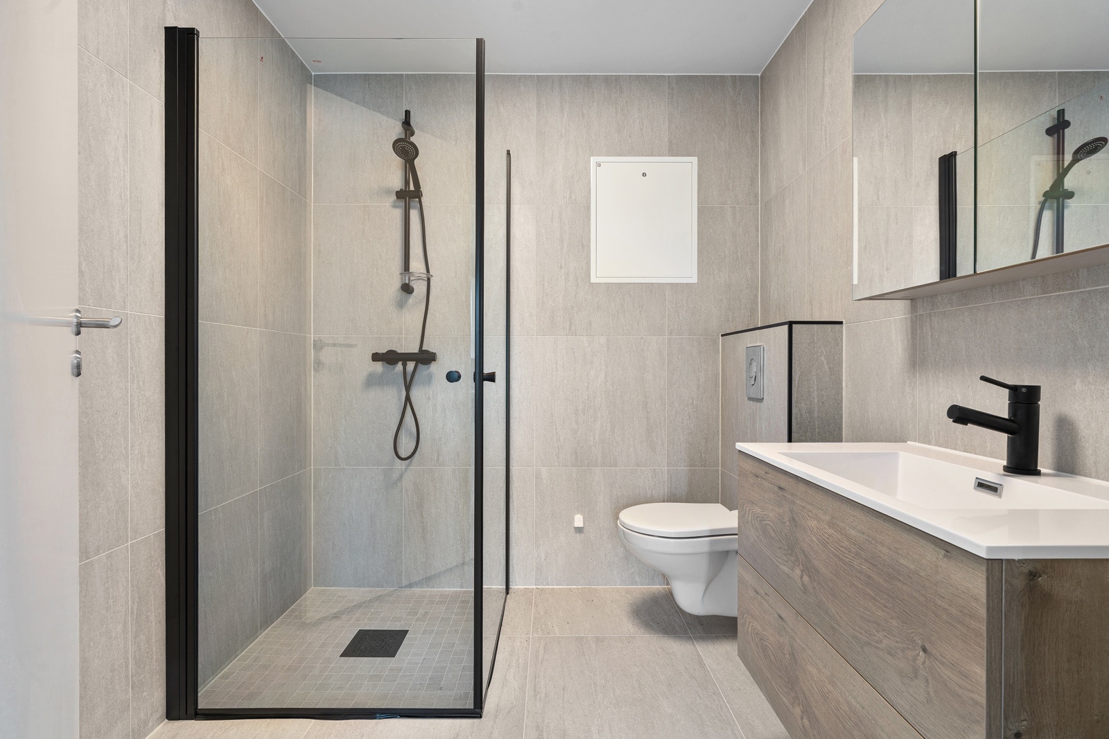 Lekkert flislagt bad med storformatflis. Moderne innredning, dusjhjørne og vegghengt toalett.