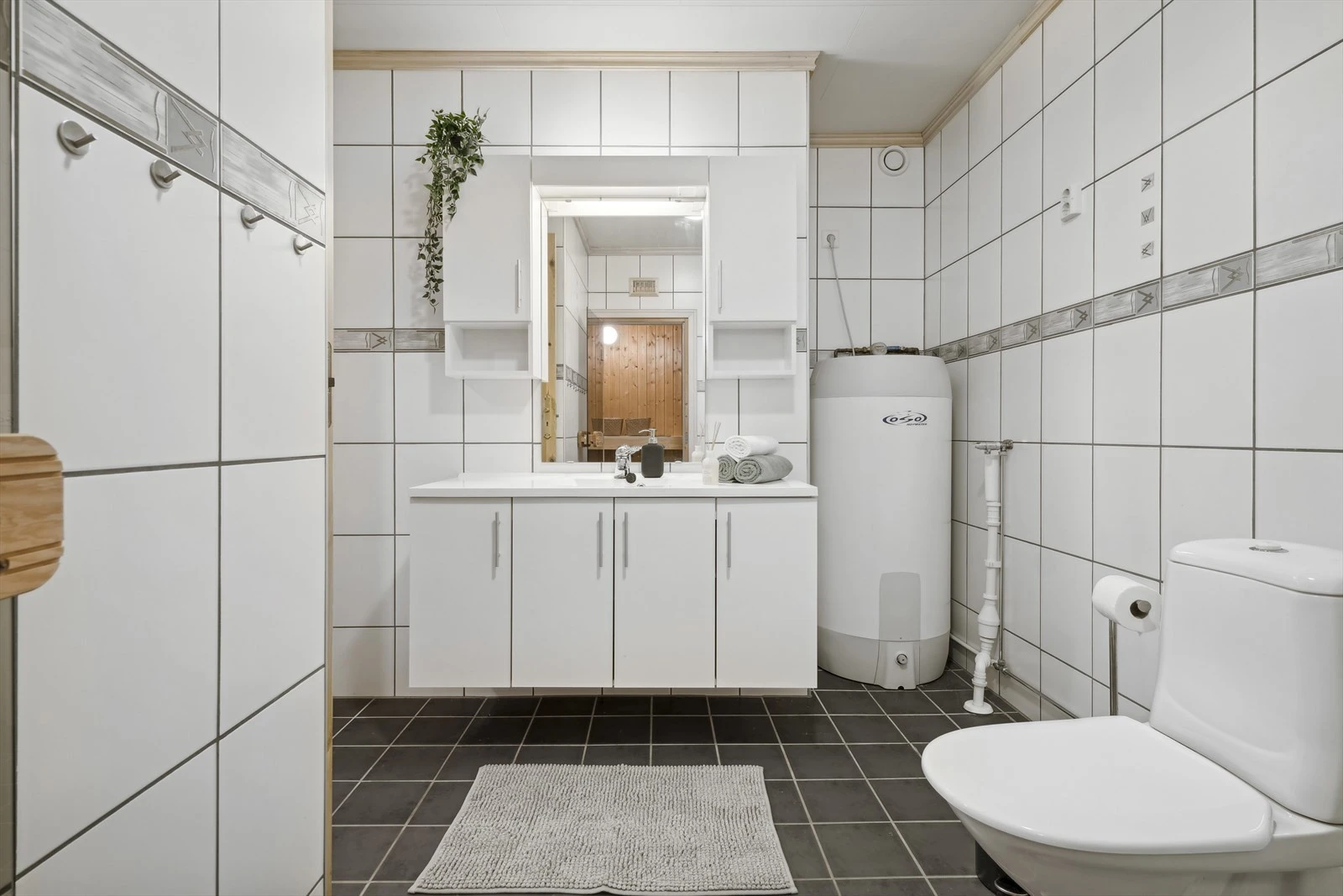 Romslig og flislagt baderom med varmekabler i gulv. Badet inneholder servantskap med hel servantplate, 2 overskap, speil med lys, wc, dusjhjørne med tett sokkel og uttak for vaskemaskin. Ventilasjon via veggventil til mekanisk avtrekk. Galleribilde