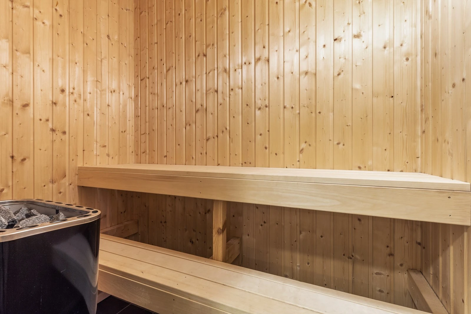 Badstua er innredet med Narvi elektrisk badstueovn og trebenker. Flislagt gulv. Granpanel på vegger og i himling. Benker av heltre. Lufting mot bad Galleribilde