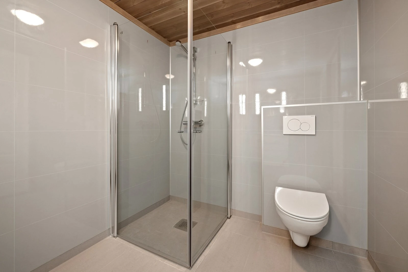 Badet er innredet med vegghengt toalett og dusjhjørne med foldedører i glass. Galleribilde