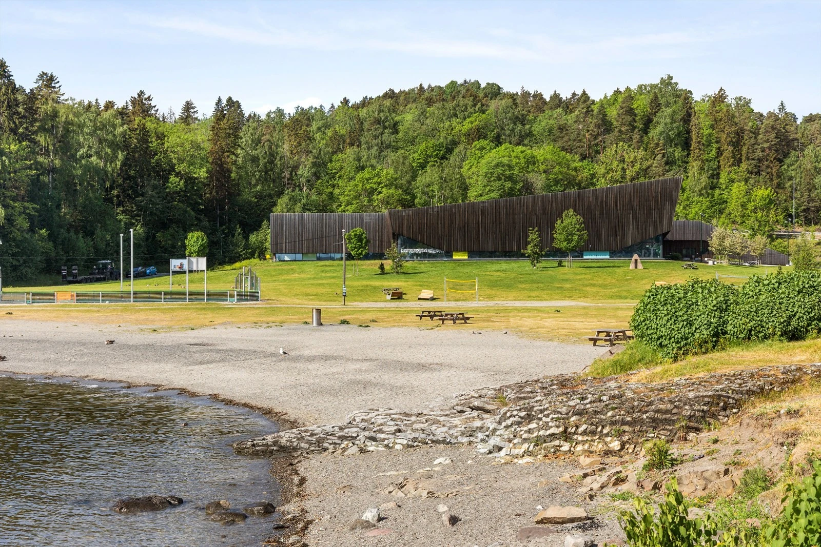 Holmenskjæret badestrand med ballbinge, sandvollyballbane, lekeapparater og Holmen svømmehall. Galleribilde