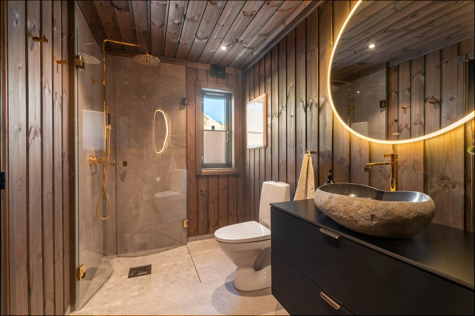 Svært lekkert baderom med flis på gulv med varmekabler, beiset panel på vegger og i himling med integrert belysning. Galleribilde