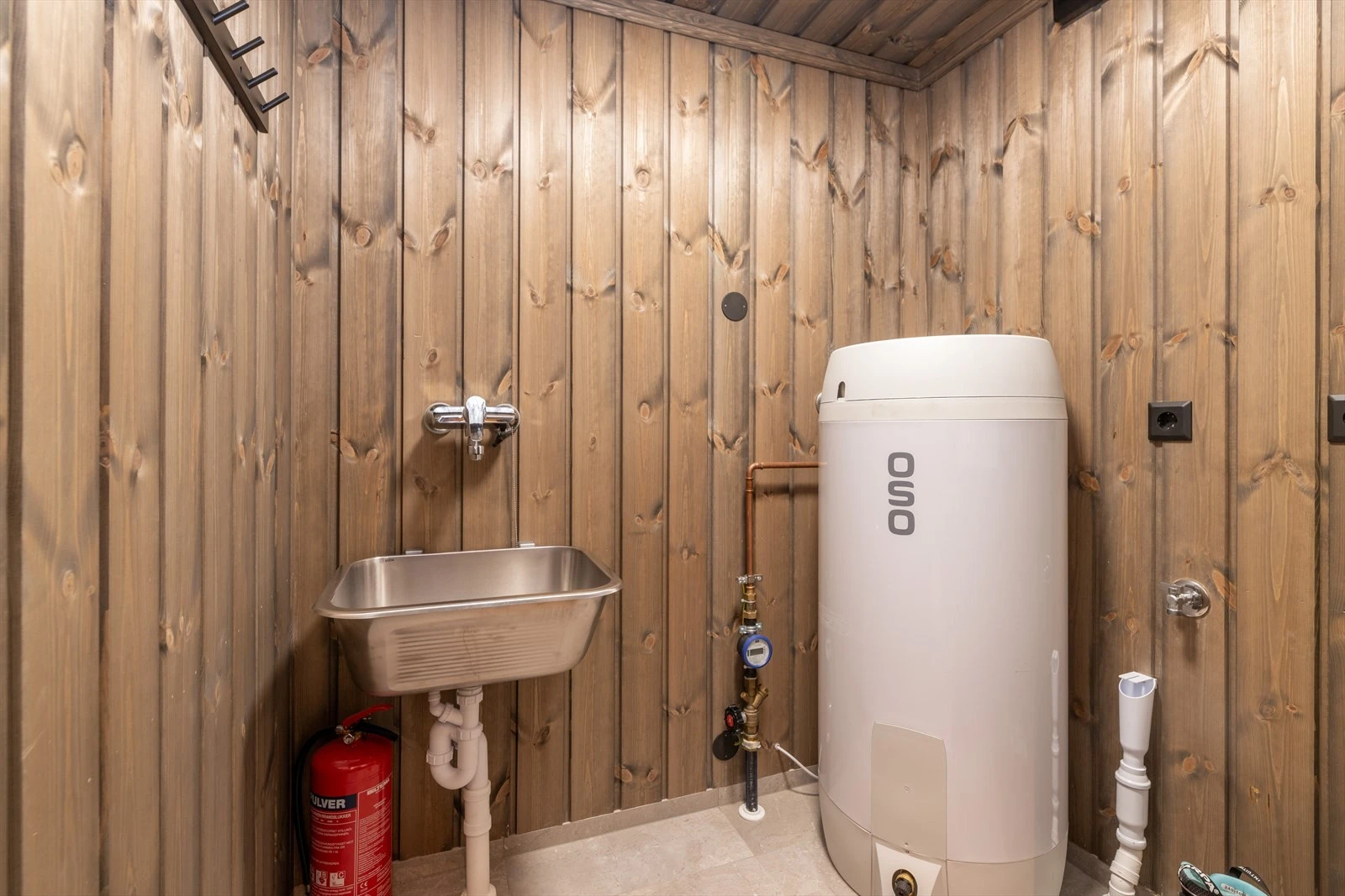 Fra baderom er det tilkomst videre inn til vaskerom/teknisk rom. Opplegg og plass for vaskemaskin, samt praktisk, veggmontert utslagsvask. Hyttas varmtvannstank er plassert i rommet og er av typen Oso på ca. 200 liter. Galleribilde