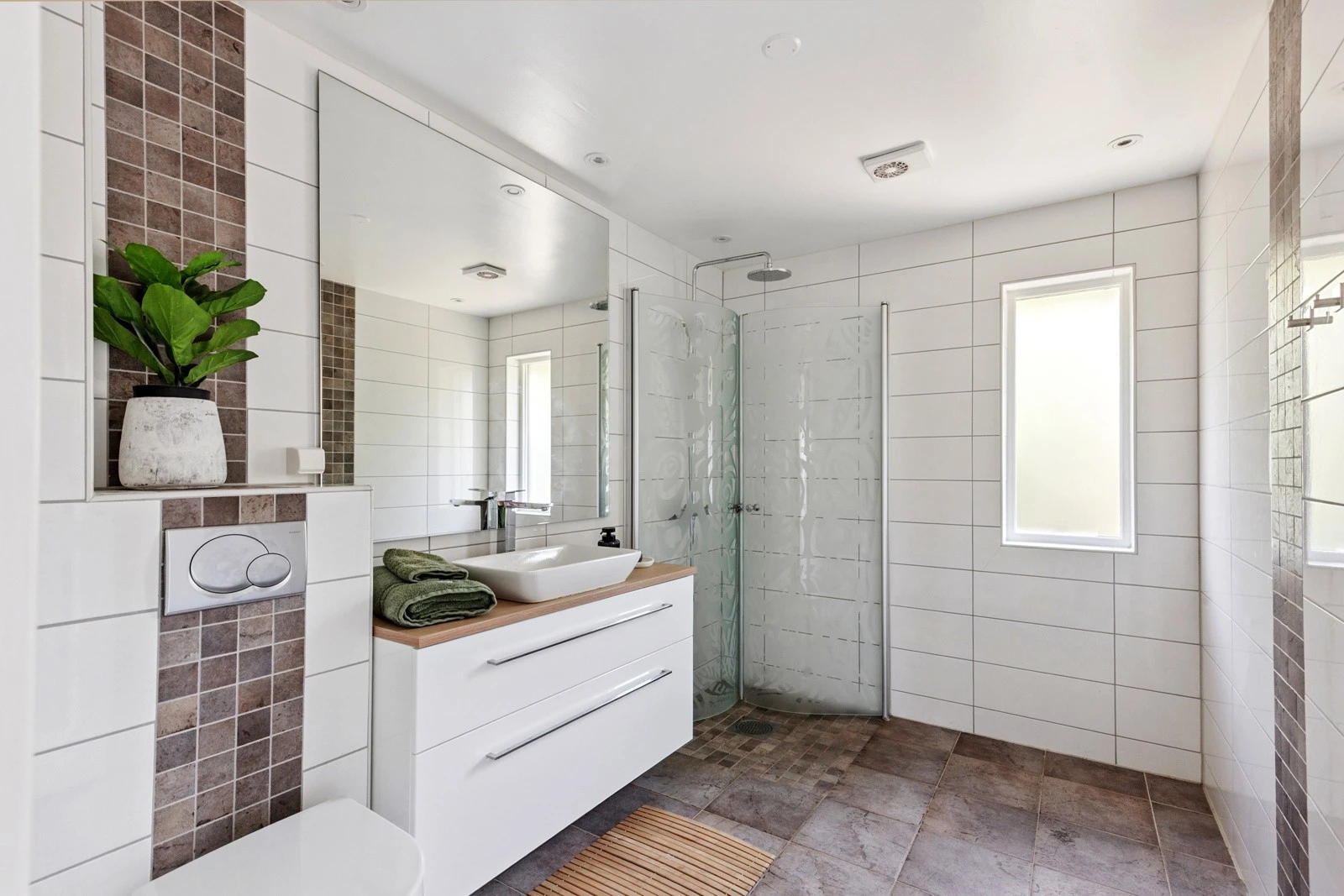 Moderne bad med fliser på både gulv og vegger, dusjhjørne og vegghengt toalett. Det er ett bad i hver etasje. Galleribilde