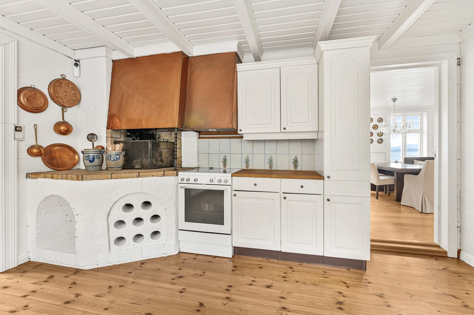 Flott peis på kjøkken med kobberhette.
Frittstående komfyr, kjøleskap og oppvaskmaskin. Galleribilde