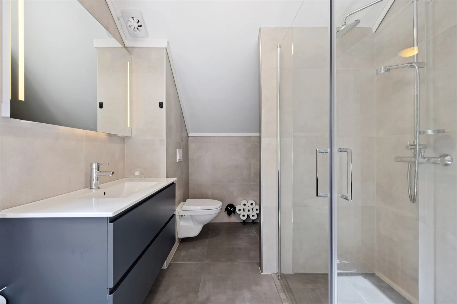 Rommet har innredning med nedfelt servant, veggmontert toalett, dusjvegger/hjørne og opplegg for vaskemaskin. Elektriske varmekabler