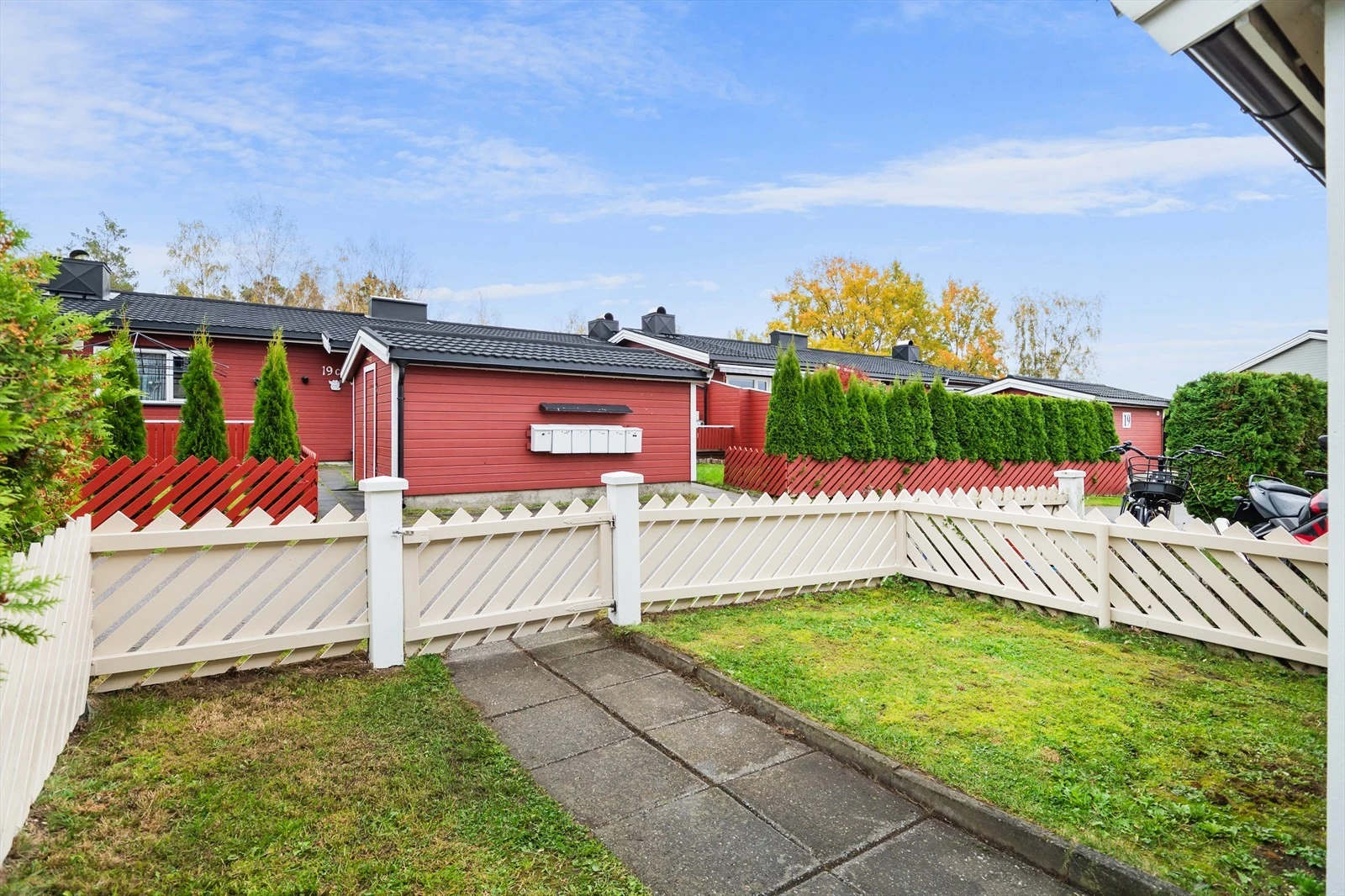 Boligen har adkomst via port til et inngjerdet frontparti med steinlagt stikkvei, gressplen og markterrasse fra 2024. Galleribilde