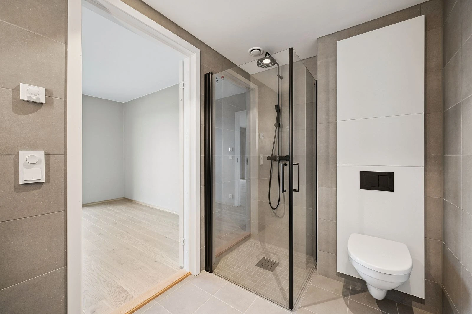 Romslig dusjnisje med glassdører og stilrent armatur.