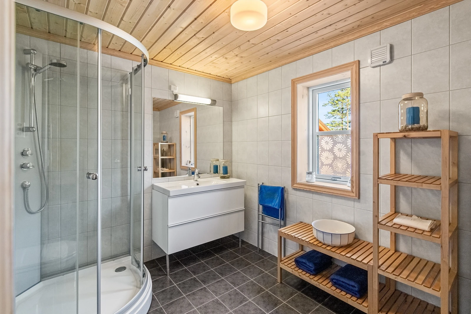 Flislagt bad med servant i innredning, dusjkabinett og vegghengt toalett Galleribilde