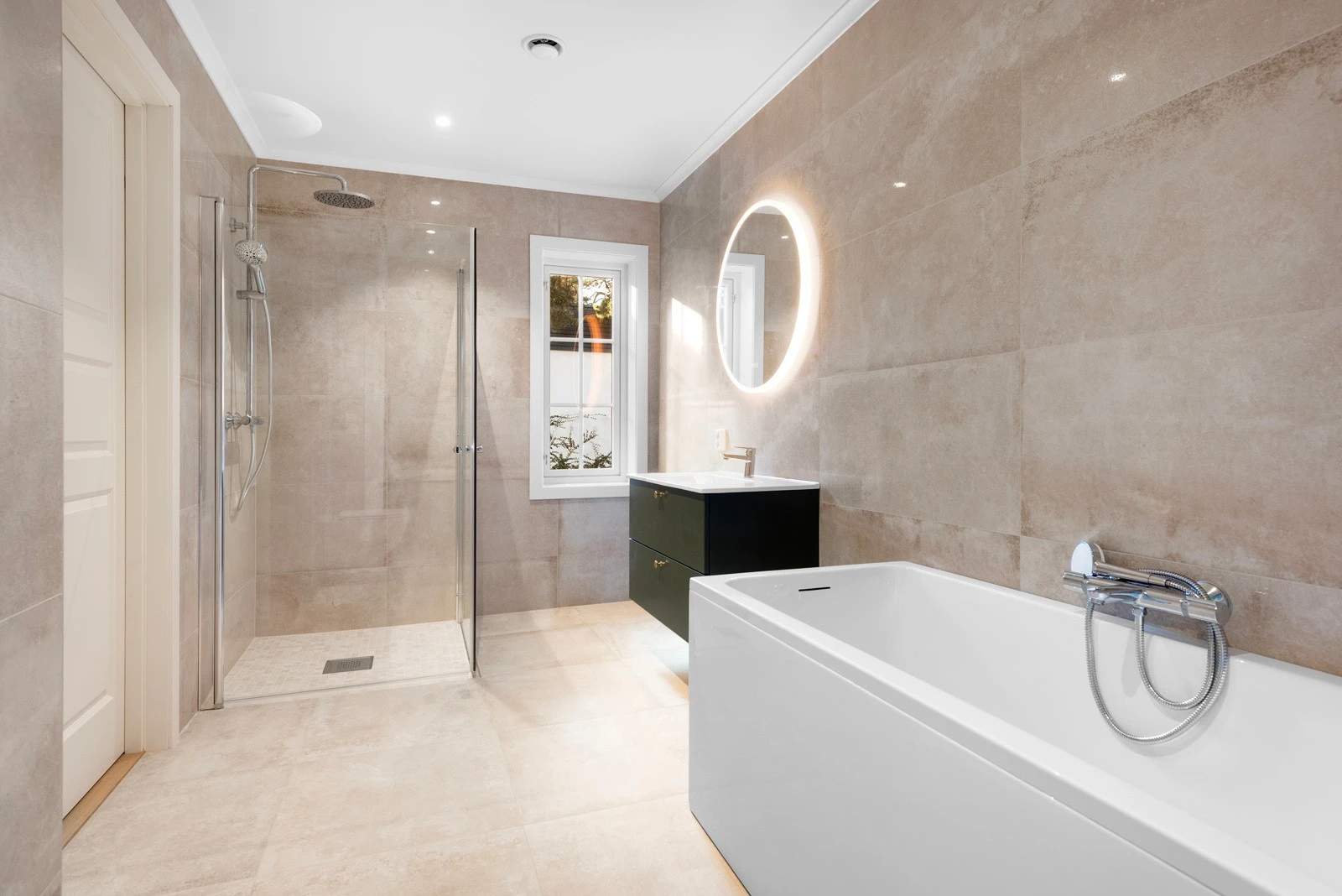 Baderommet har et eksklusivt servantskap og et stilrent rundt speil fra Strai med lys bak, samt en 100 x 100 cm dusj, badekar og store fliser opp til taket, som sammen skaper en moderne og luksuriøs atmosfære Galleribilde