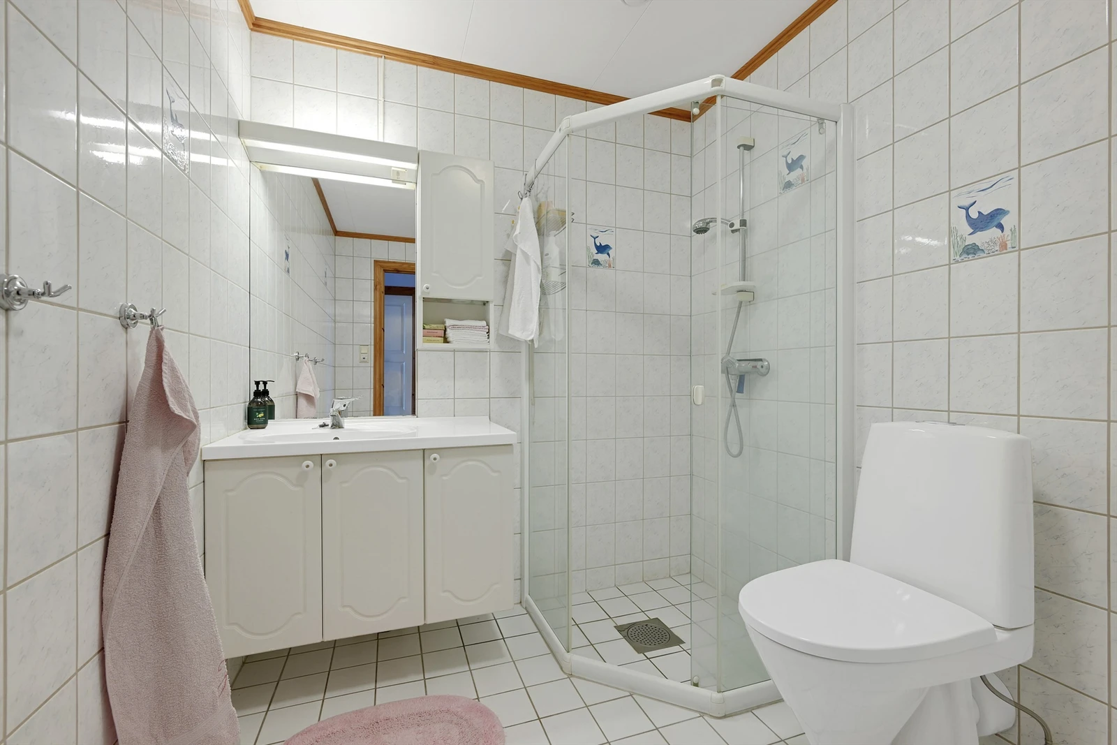 Flislagt badeværelse med dusjhjørne, håndvask i innredning med speil og overskap, wc og plass/opplegg for vaskemaskin Galleribilde