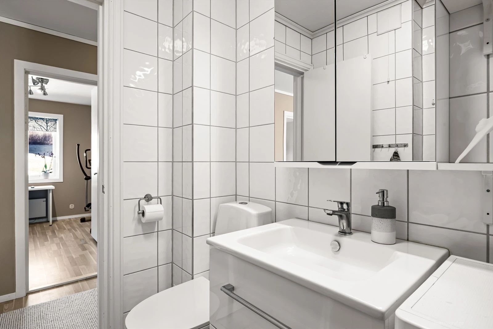 Pent flislagt bad med innredning bestående av klosett, dusjhjørne og baderomsinnredning med speilskap.