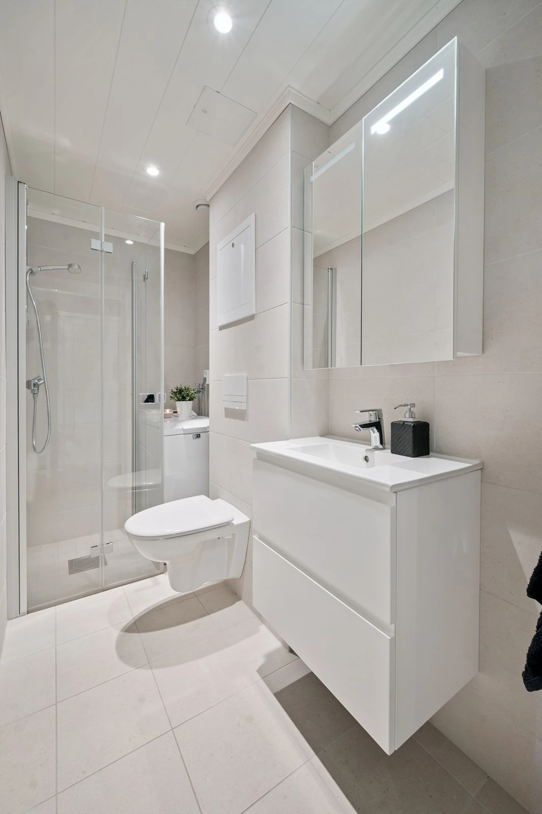 Rommet har innredning med nedfelt servant med skuffer, speilskap, veggmontert toalett, dusjvegger/hjørne og opplegg for vaskemaskin.