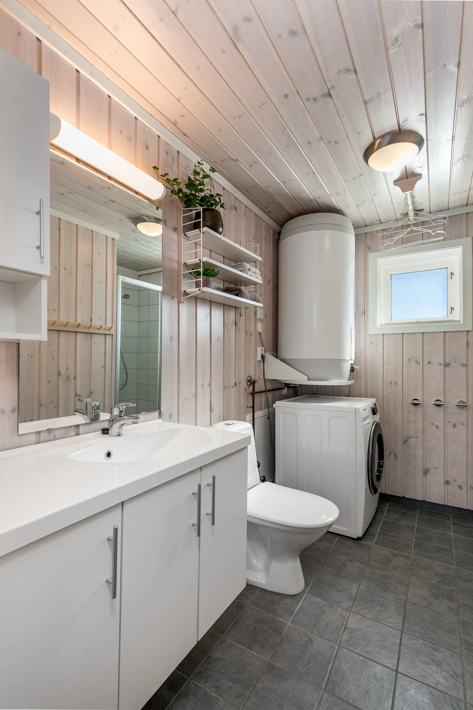 Bad 1 med flislagte gulv og dusjsoner, hvitpigmentert panel på vegger. Baderomsinnredning bestående av benkeskap og veggskap med glatte fronter. Speil og belysning over servant. Opplegg for vaskemaskin. Galleribilde