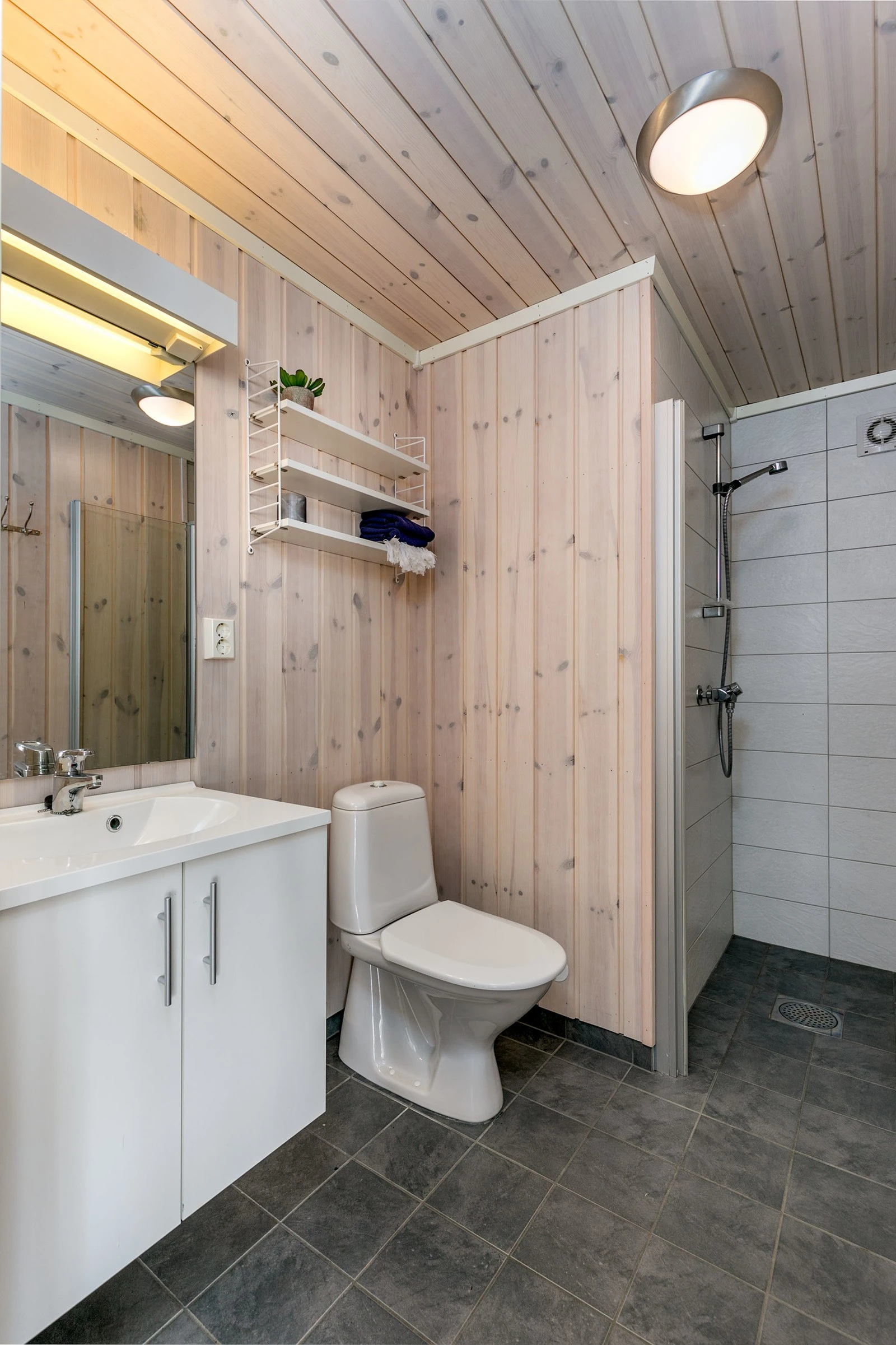 Bad 2 med flislagte gulv og dusjsoner, hvitpigmentert panel på vegger. Baderomsinnredning bestående av benkeskap med glatte fronter. Speil og belysning over servant. Dusjnisje med innfellbar dør i herdet glass, servant i helstøpt plate og gulvstående wc. Galleribilde