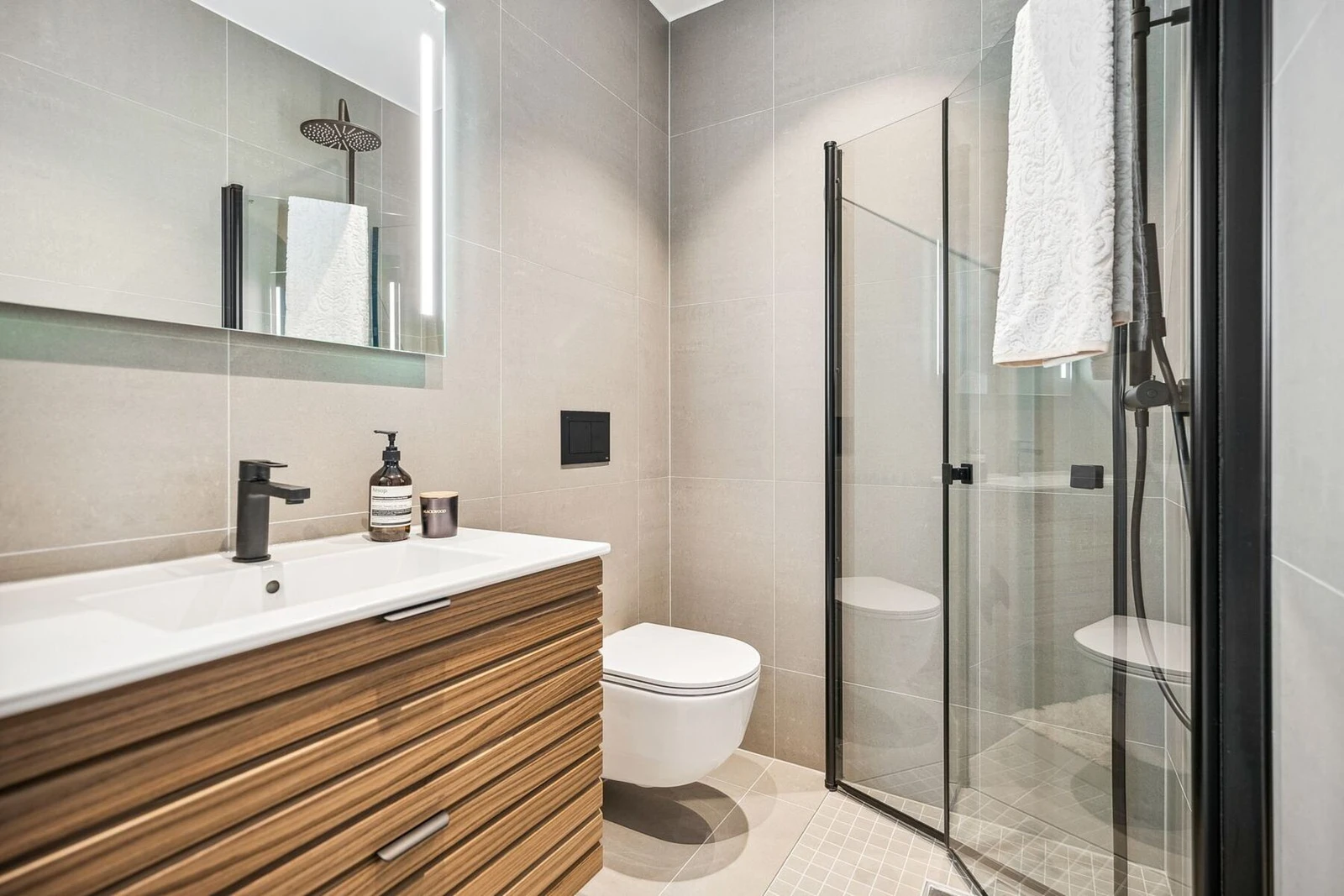 Bad 2 i 1. etasje har varme i gulv og er innredet med dusj med innfellbare dører i herdet glass, benkeskap med glatte fronter, servant, speil med belysning over servant og vegghengt toalett med innebygget sisterne. Galleribilde