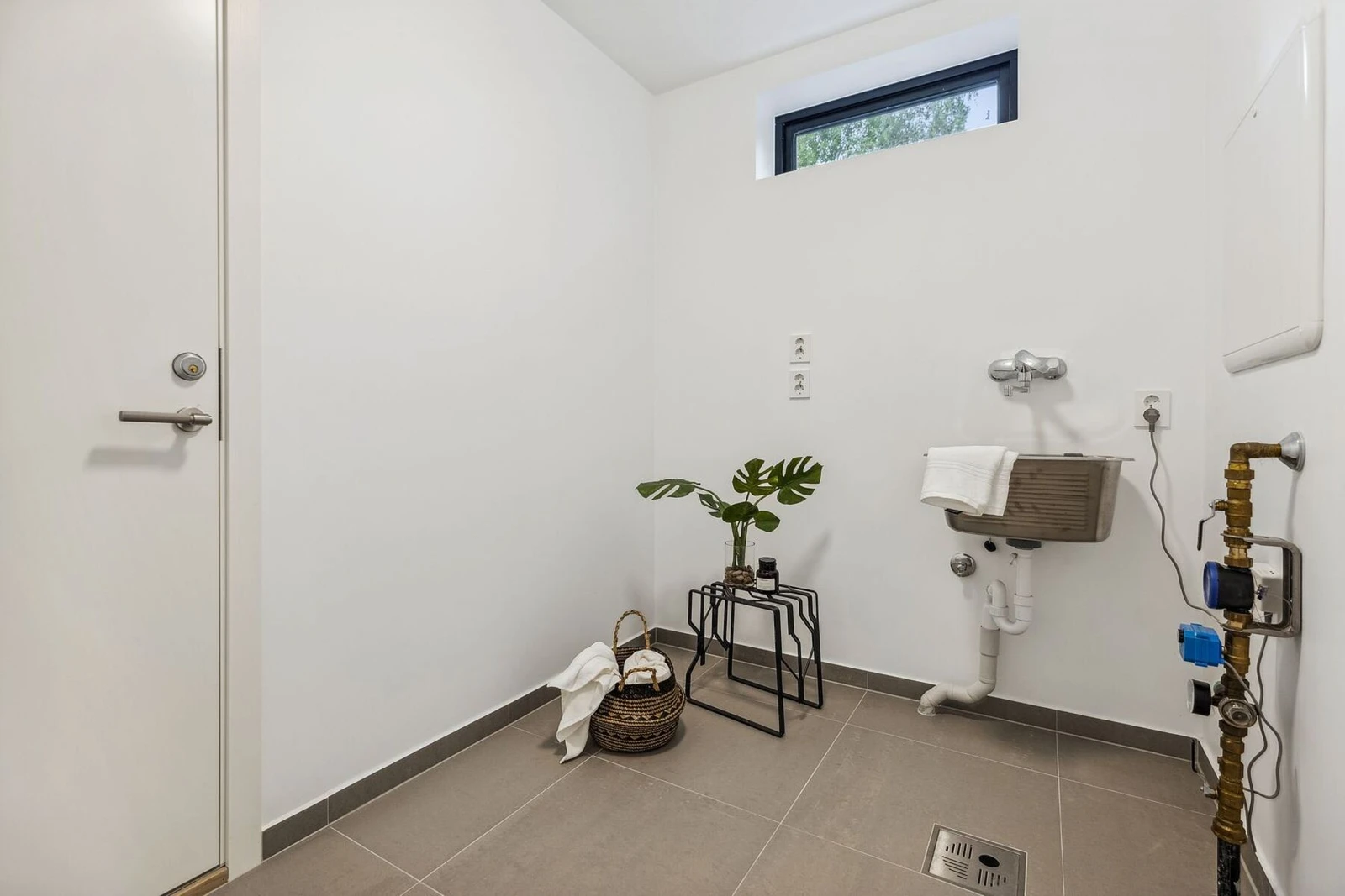 Praktisk vaskerom med fliser på gulv med gulvvarme og malte plater på vegg. Skyllekum i rustfritt stål og
opplegg for vaskemaskin. Galleribilde