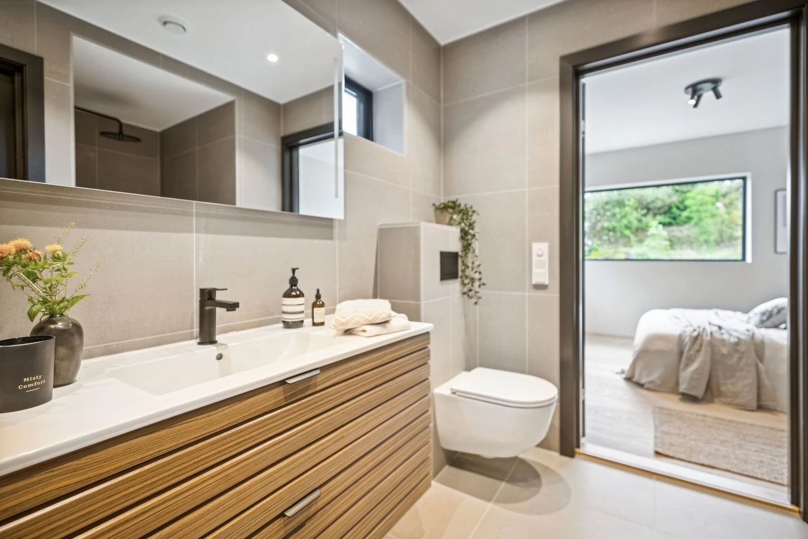 Badet er utstyrt med dusjinisje samt dusj i badekar, benkeskap med glatte fronter, servant, speil med belysning over servant og vegghengt toalett med innebygget sisterne. Galleribilde