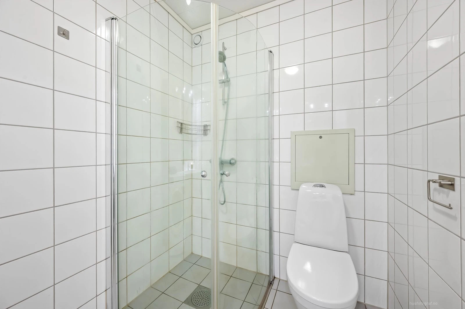 Pent flislagt bad med innredning bestående av klosett, dusjhjørne og baderomsinnredning med speilskap.
