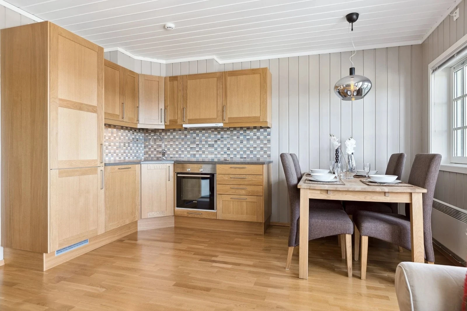 Stilrent kjøkken innredet med malte skrog og fronter, laminat benkeplater og fliser mellom benk og overskap Galleribilde