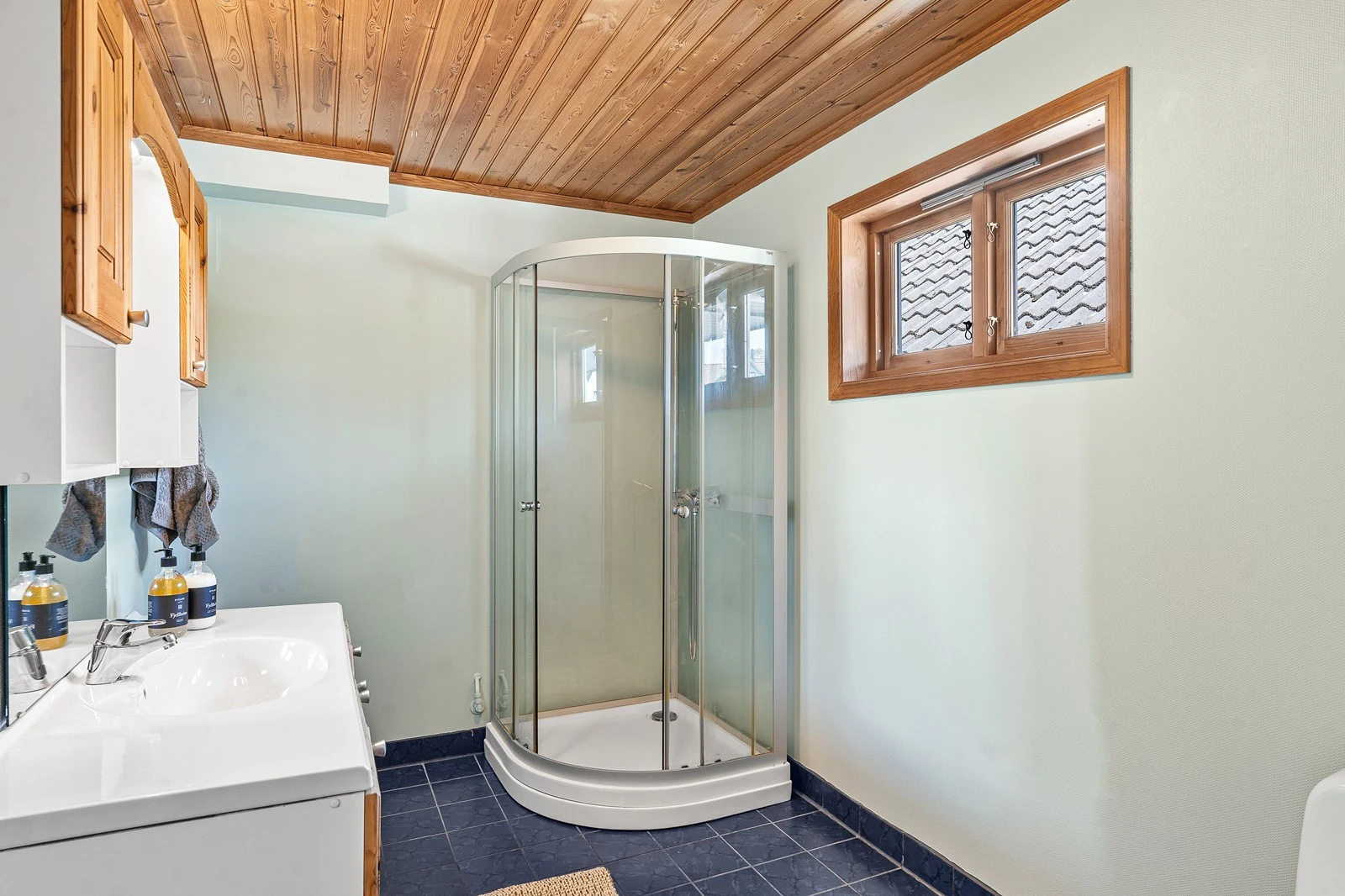 Badet i 1. etasje har flislagt gulv med varmekabler, mens veggene er dekket med tapetserte plater. Galleribilde