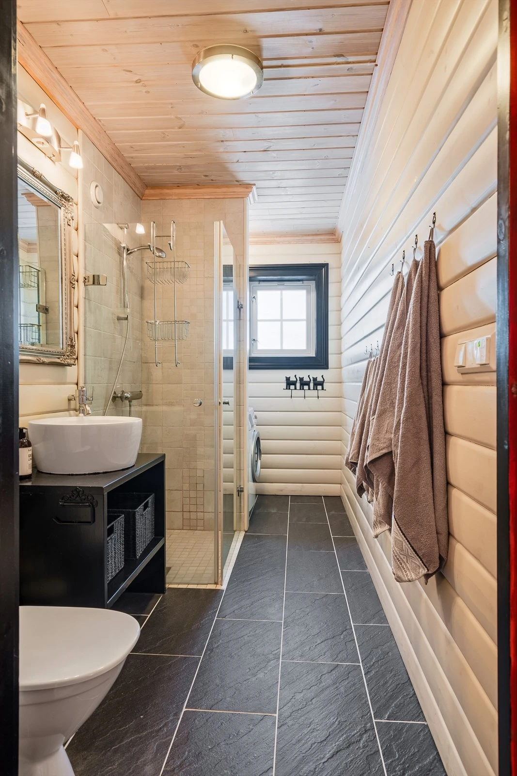 Baderom 1 er et lyst og pent baderom med flislagt gulv med gulvvarme og panel på veggene kombinert med fliser i dusjsonen. Innerst i rommet er det en praktisk nisje med plass og opplegg for vaskemaskin. Galleribilde