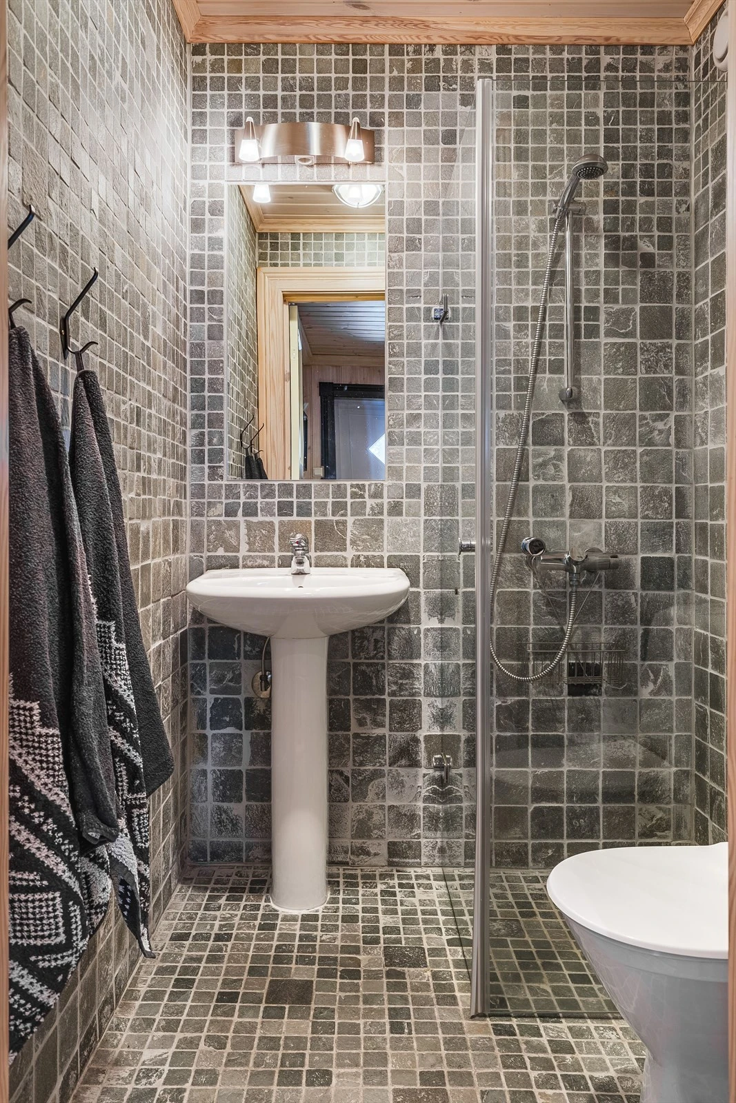 Baderom 2 har flotte fliser på gulv og vegger, deilig gulvvarme og mekanisk avtrekk. Baderommet er utstyrt med søyleservant med speil og belysning over, dusjhjørne med glassdører og gulvstående toalett. Galleribilde