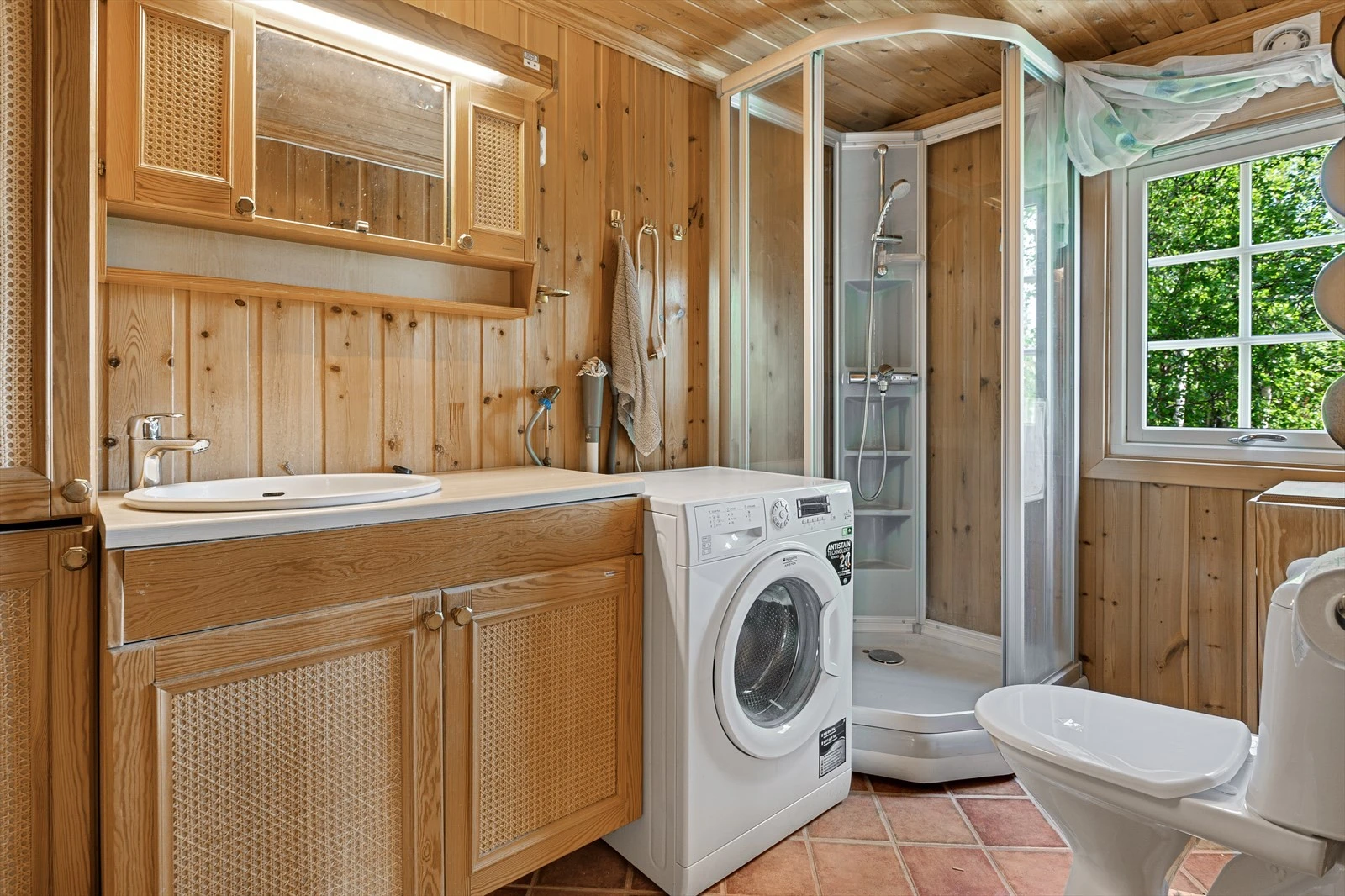 Bad med klosett, servant, dusjkabinett og opplegg til vaskemaskin. Baderomsinnredning i folierte plater med over-og underskap og høyskap, laminat benkeplate. Speil med belysning på overskap. Galleribilde