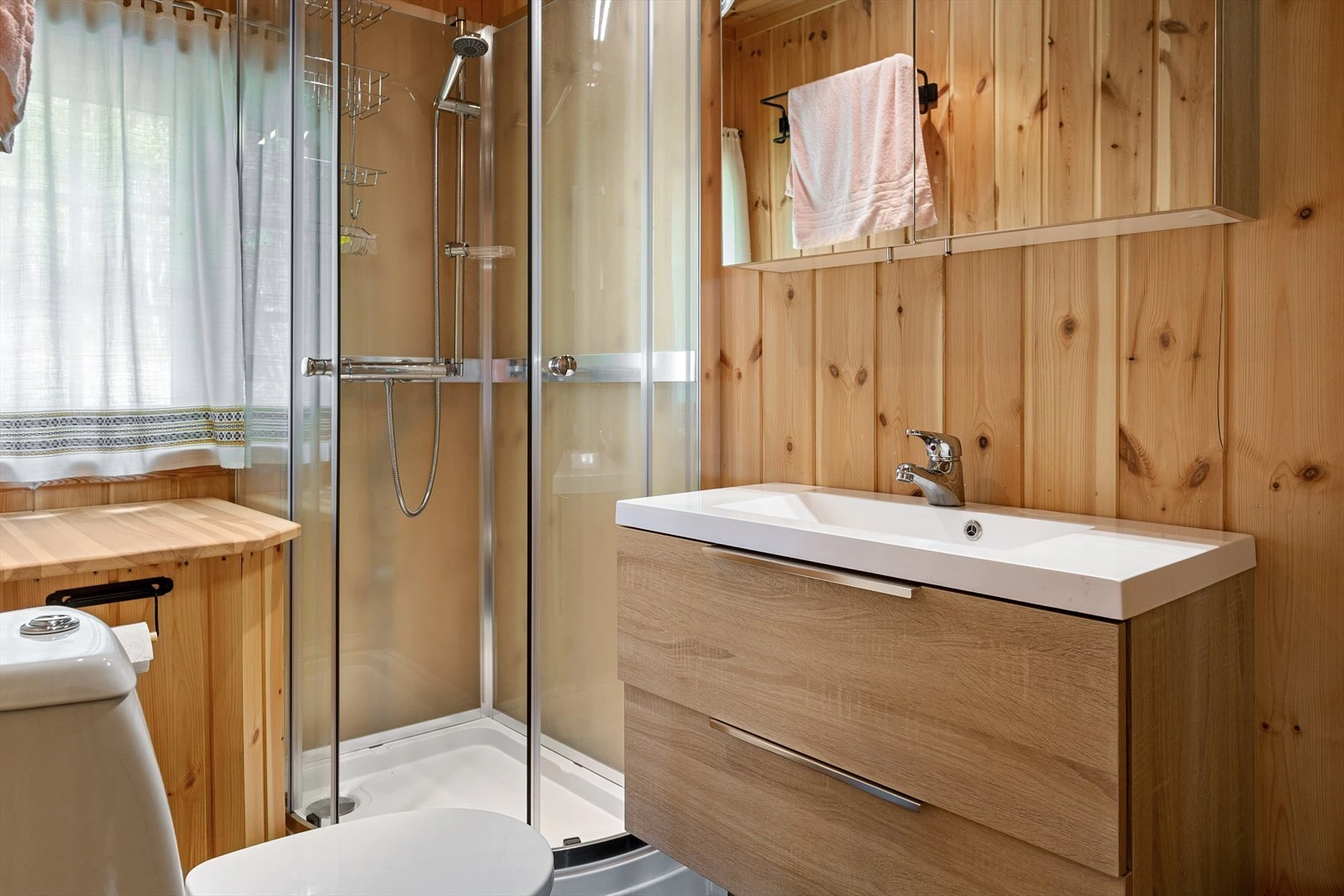 Bad med klosett, servant og dusjkabinett. Baderomsinnredning i folierte plater med over-og underskap og høyskap, speil med tilhørende belysning på overskap. Galleribilde