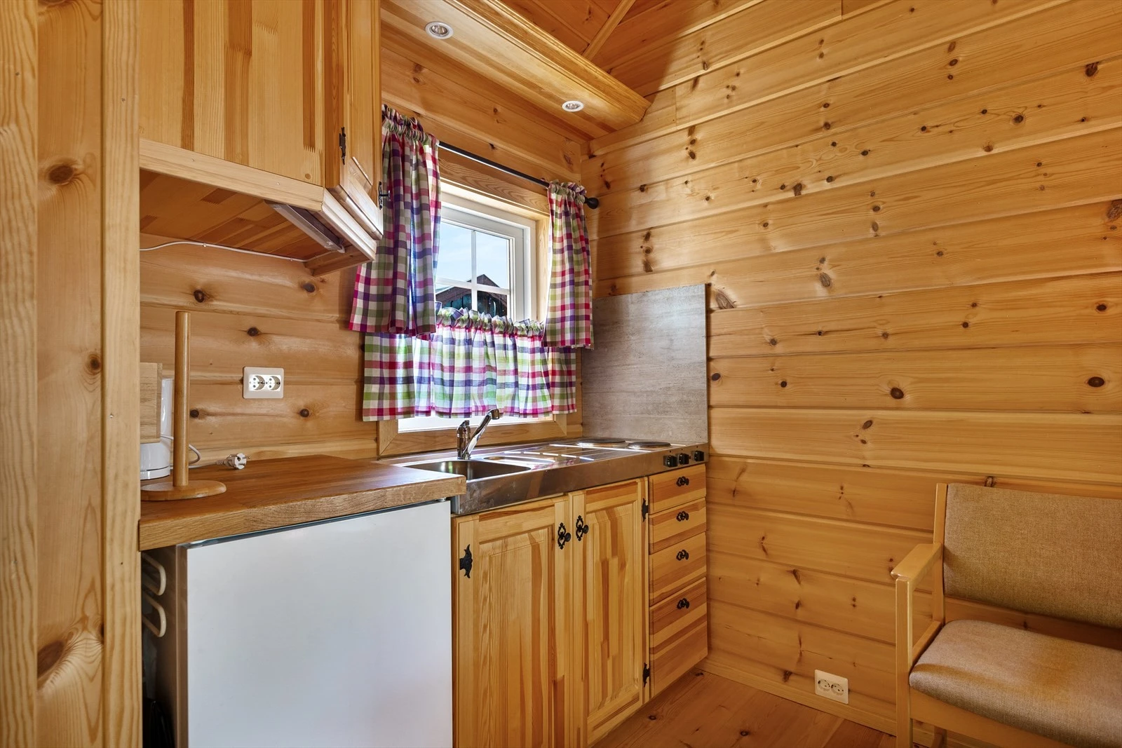 Liten kjøkkeninnredning av heltre, med heltre benkeplate. Kombinert oppvaskkum med kran og kokeplate med benk i stål. Galleribilde