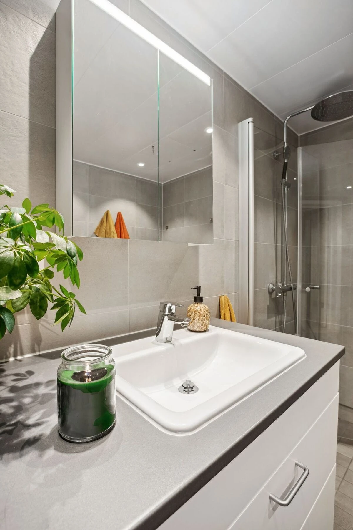 Speilet med integrert belysning gir et praktisk og stilrent uttrykk, mens planter og dekorative elementer tilfører en lun atmosfære. Galleribilde
