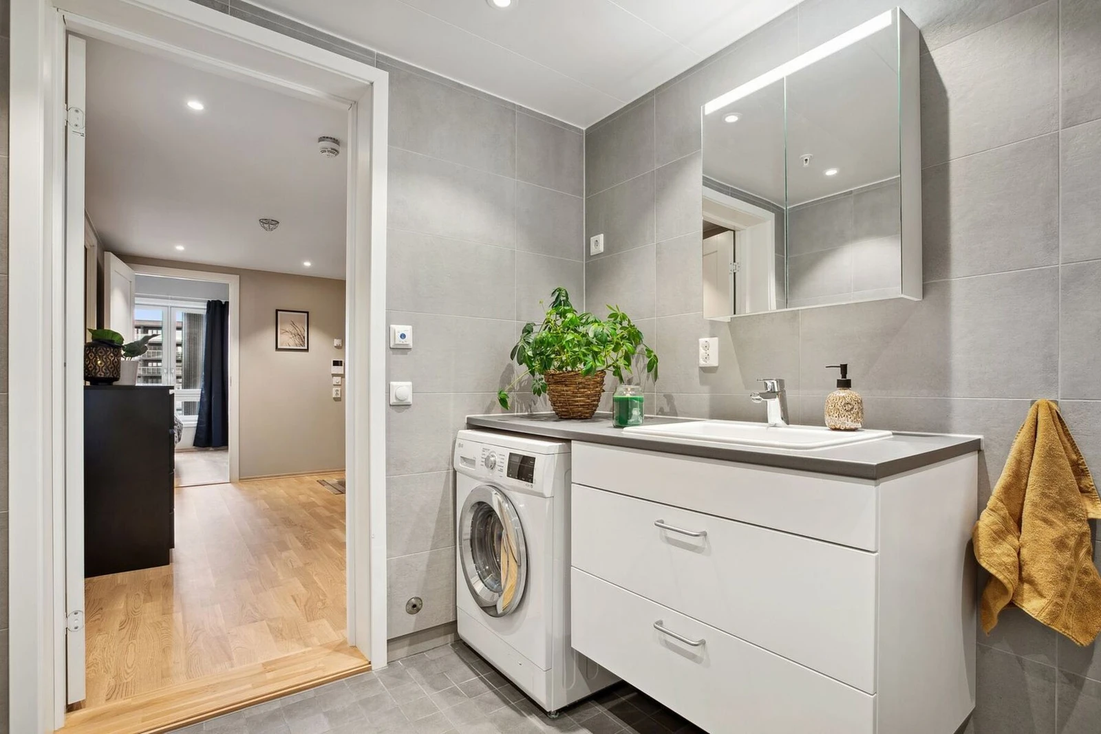 Med vaskemaskin integrert under benkeplaten blir badet også svært funksjonelt. Åpningen mot gangen gir en naturlig flyt mellom rommene og understreker leilighetens gode planløsning. Galleribilde