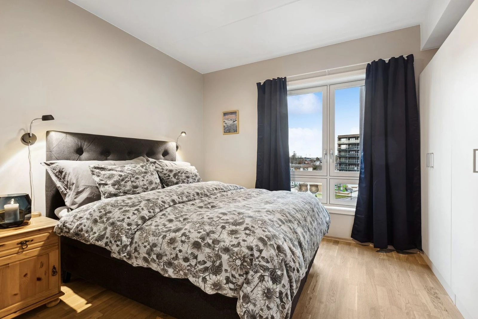 Hovedsoverom med lune og harmoniske farger, hvor naturlig lys fra store vinduer gir rommet en innbydende atmosfære. Den komfortable dobbeltsengen, med polstret sengegavl og vakre tekstiler, danner et naturlig midtpunkt i rommet. Galleribilde