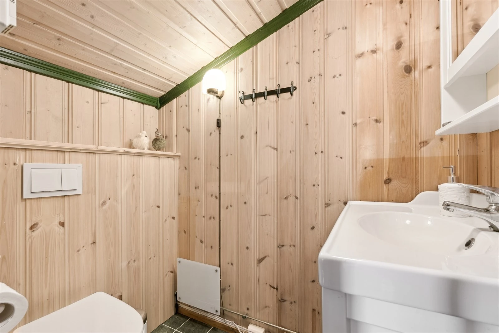 På toalettrommet er det flislagt gulv med varmekabler. Baderomsinnredning i folierte plater med underskap, servant og overskap med speil. Vegghengt toalett. Galleribilde