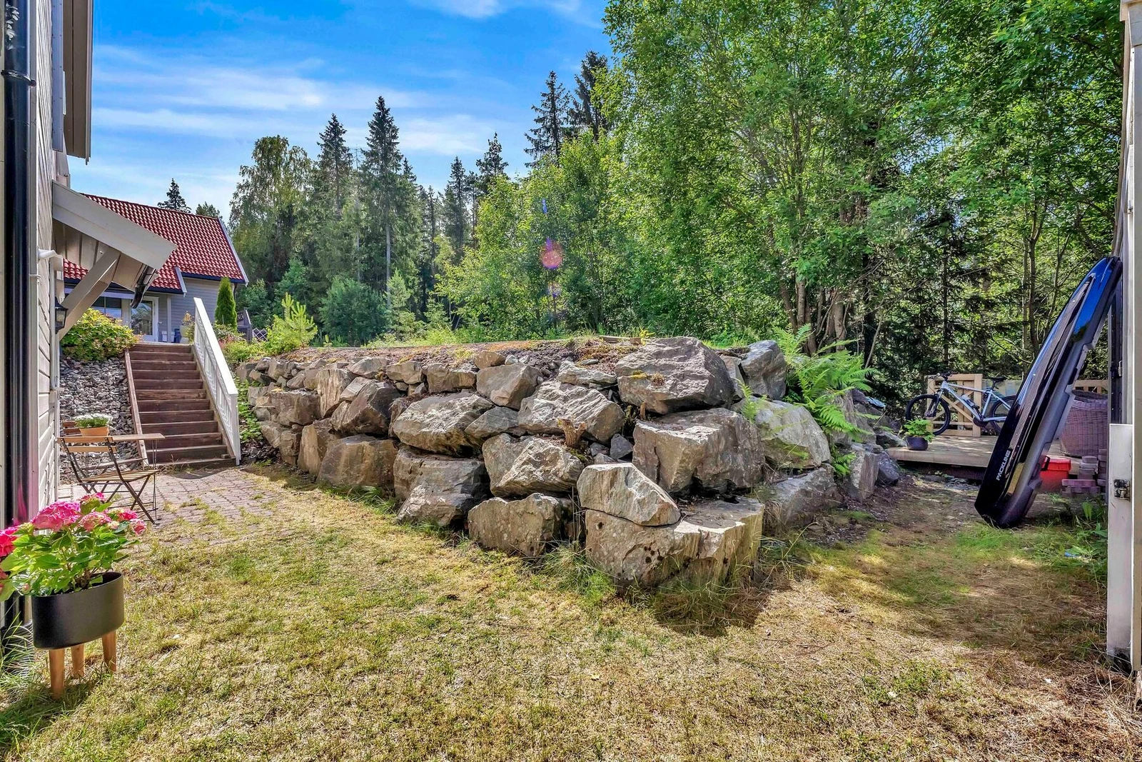 Utearealene ved inngangspartiet. To parkeringsplasser på rekke nærmest skogen tilhørende leiligheten over steinmuren. Galleribilde