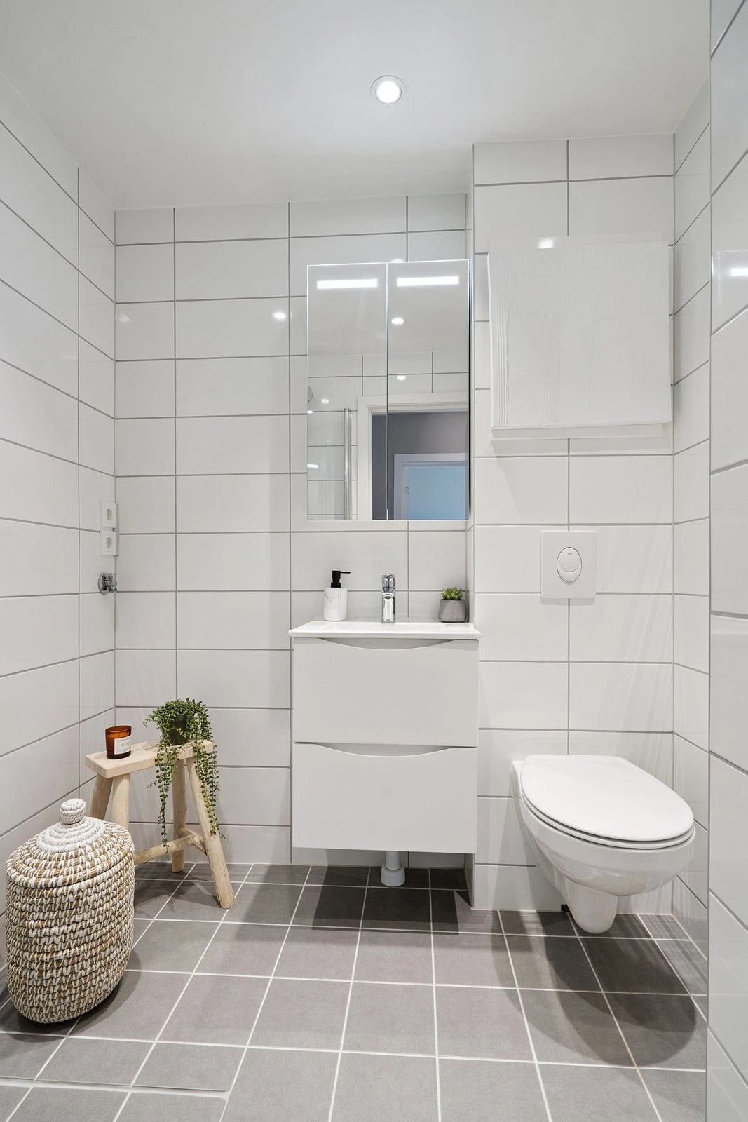 Stilrent bad med downlights i tak, fliser på gulv og vegger, og smarte oppbevaringsløsninger.