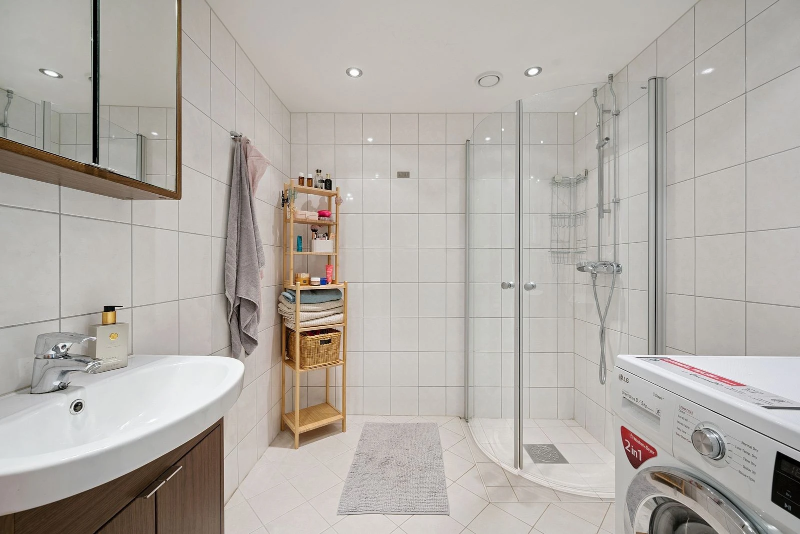 Delikat baderom med lyse fliser, moderne innredning og opplegg for vaskemaskin.