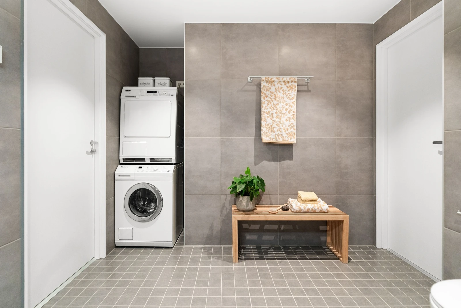 Det er opplegg for vaskemaskin og tørketrommel i nisje. Store fliser på vegg. Galleribilde