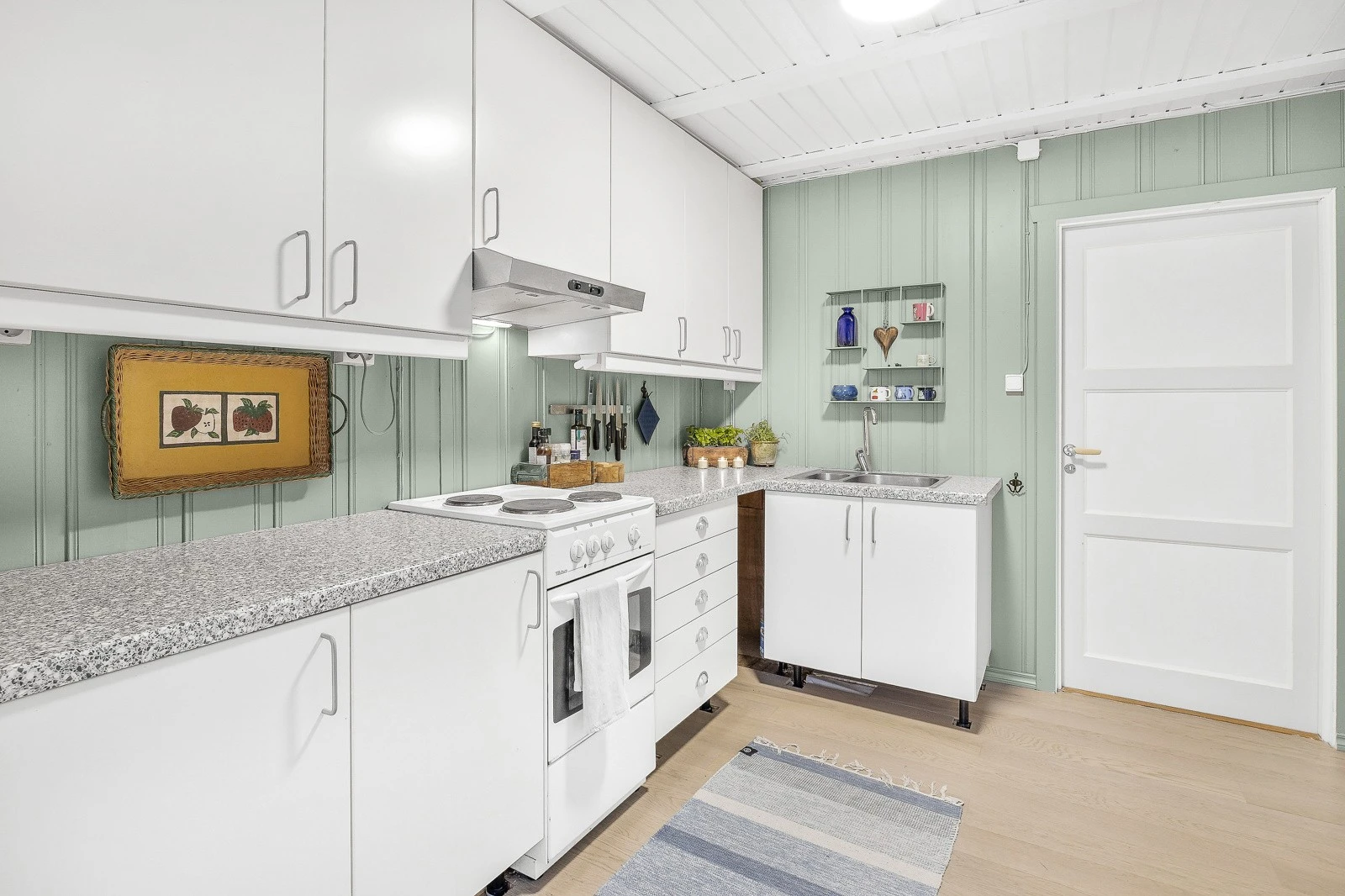 Innredning med slette fronter og benkeplater av laminat, nedfelt oppvaskkum, frittstående komfyr og kjøleskap. Galleribilde