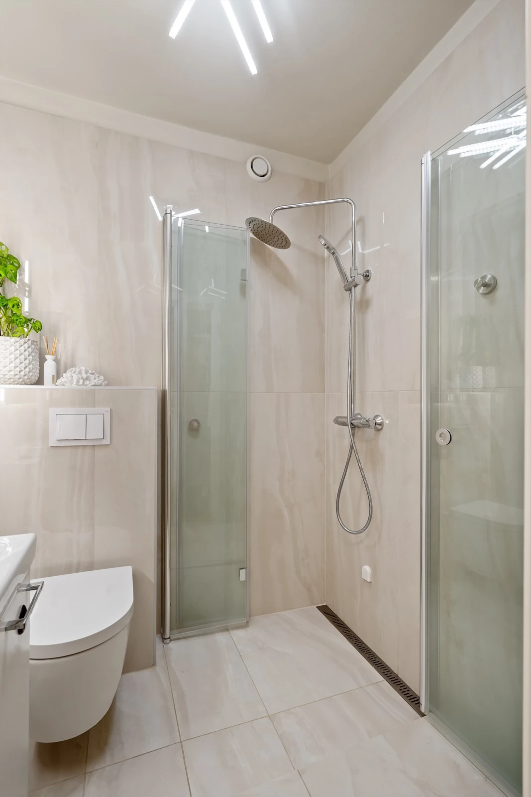 Dusjhjørne med takdusj og vegger i herdet glass, slukrenne i rustfritt stål ved vegg i dusjsonen. Galleribilde