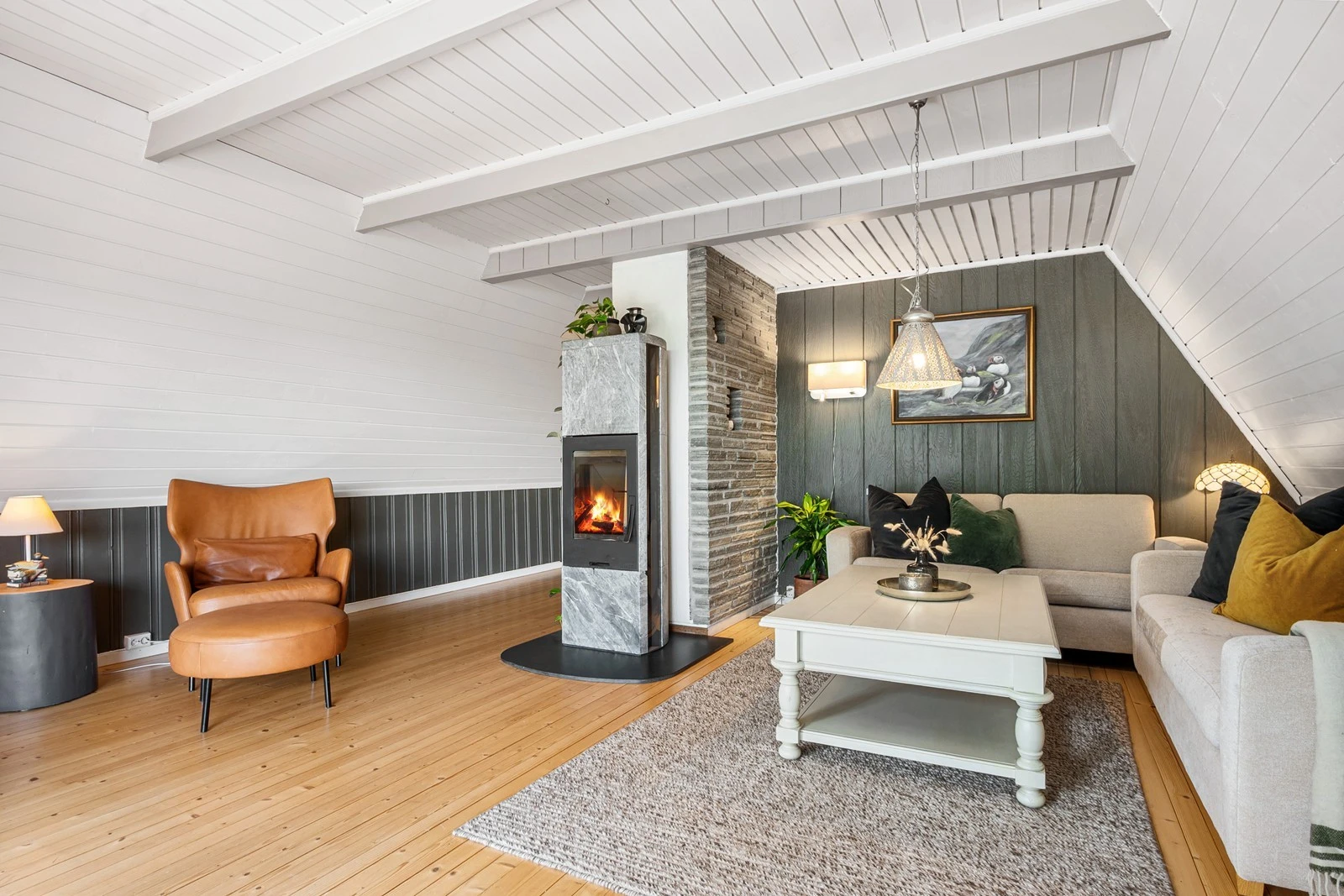 Stuen har heltre gulv, panel på vegger og en flott klebersteinspeis er plassert midt i rommet. Her er det plass til sofagruppe, lesekrok og TV-løsning. Galleribilde