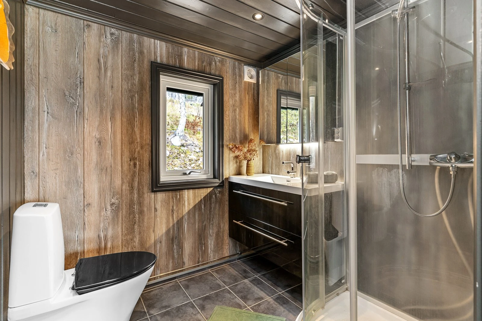 Baderommet har flislagt gulv med varmekabler, toalett, dusjkabinett, og en skuffinnredning med heldekkende servant over. Spotter i himling. Speilskap for ekstra plass til baderomsartikler. Galleribilde