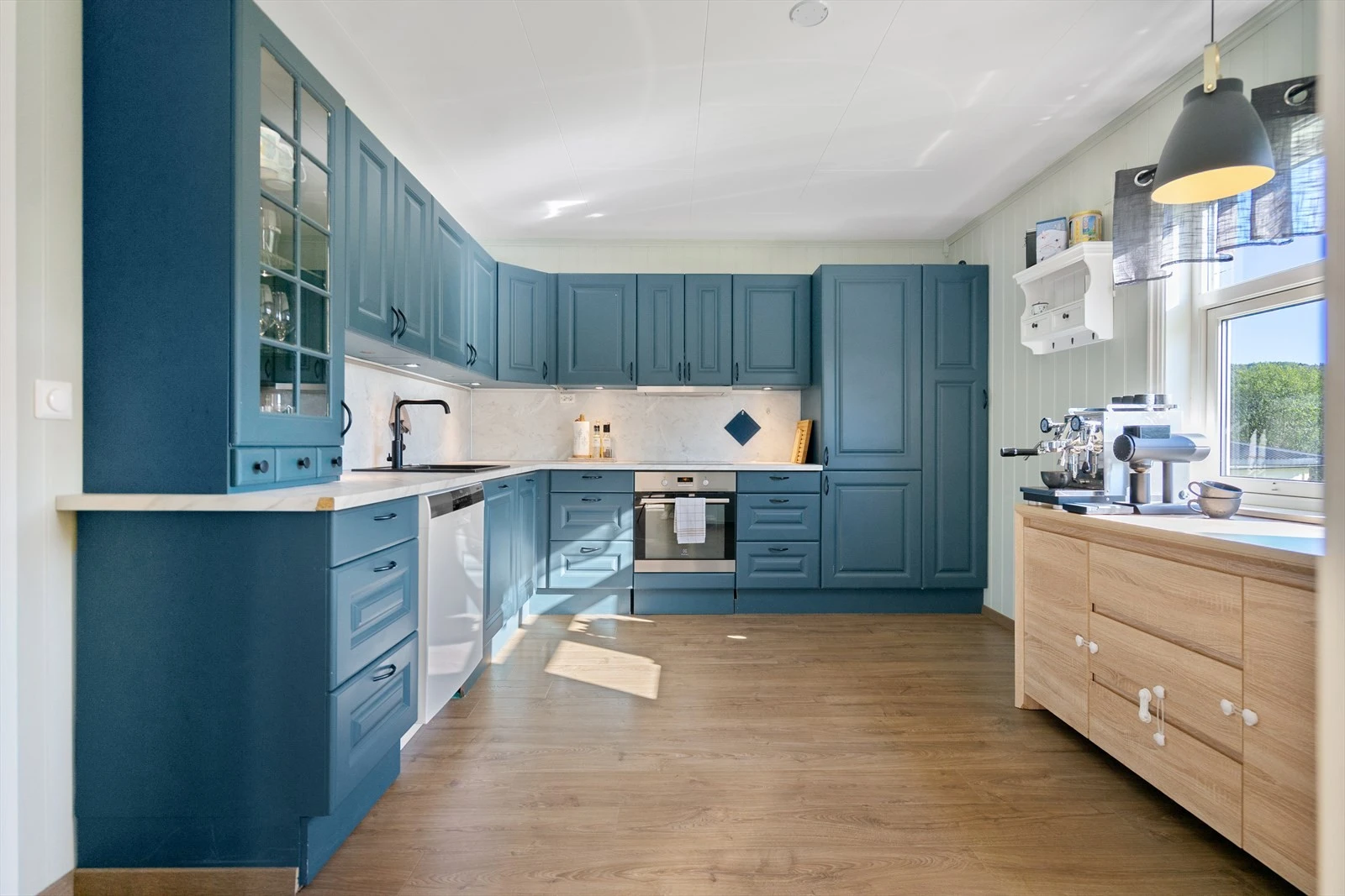 Kjøkkenet har en stilren kombinasjon av blå fronter, lyse benkeplater og integrerte hvitevarer - en flott balanse mellom funksjonalitet og design Galleribilde